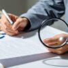 Une personne examine un contrat avec une loupe.